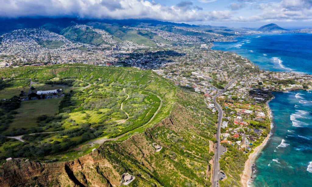 Oahu from an aeriel view, showing the large forest, coastal buildings, shoreline, and ocean. 