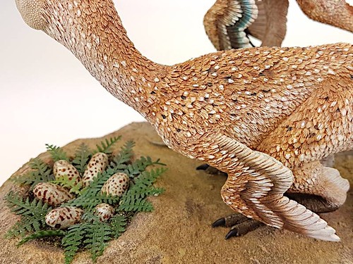 A sculpted and painted 3D rendering of a troodon protecting its nest on the ground