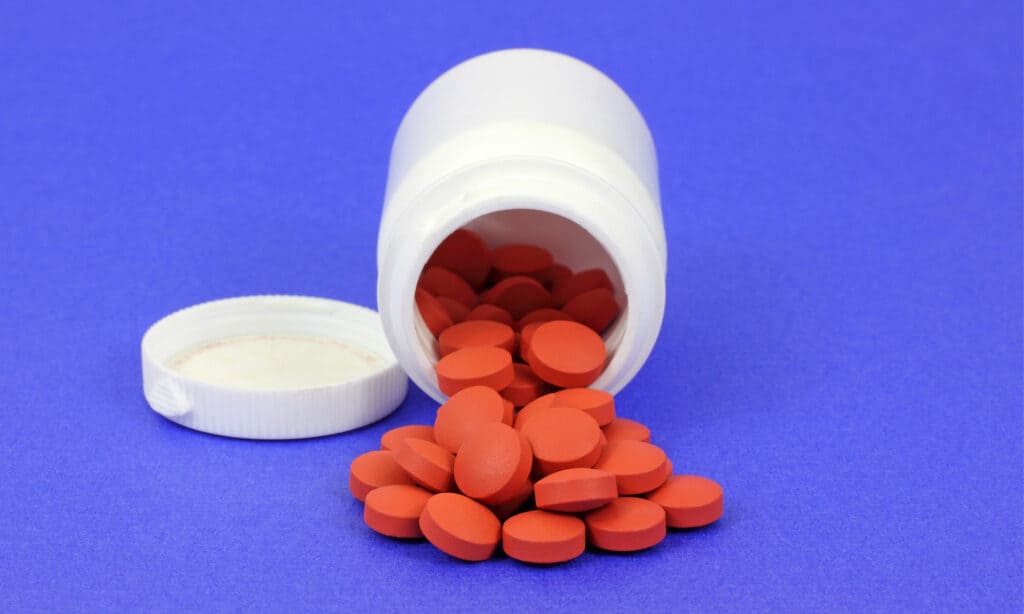 Generic ibuprofen tablets spilling out of an open bottle on a blue background