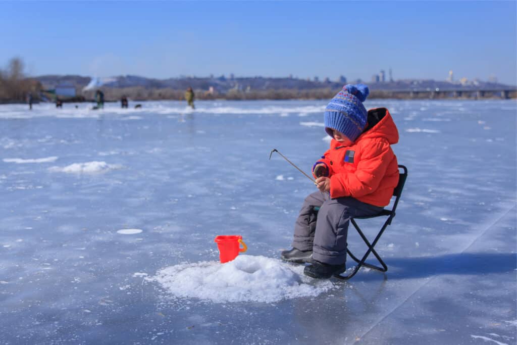 A frosty winter scene with a young boy ice fishing, highlighting the enjoyment of winter fishing for northern pike.