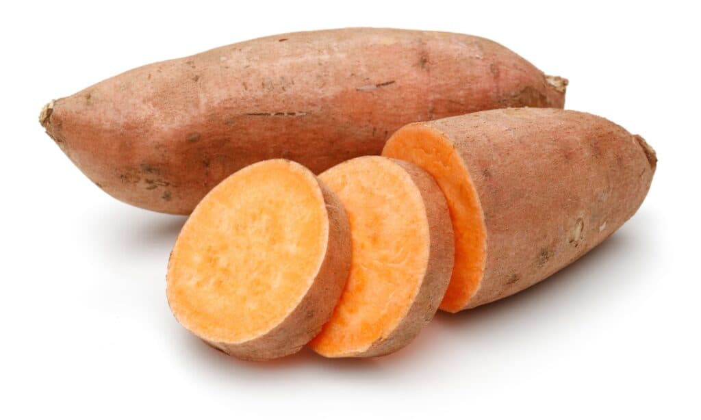 a whole sweet potato behind a partially sliced sweet potato against a white background.