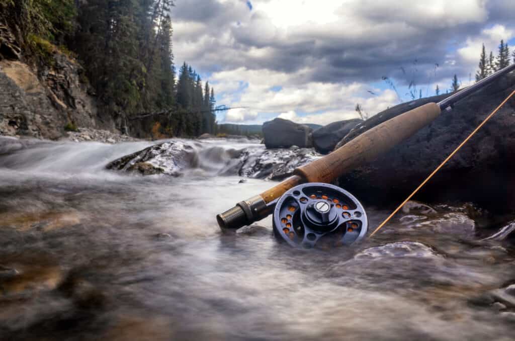 A fly fishing pole lays across the rocks in a flowing mountain stream.