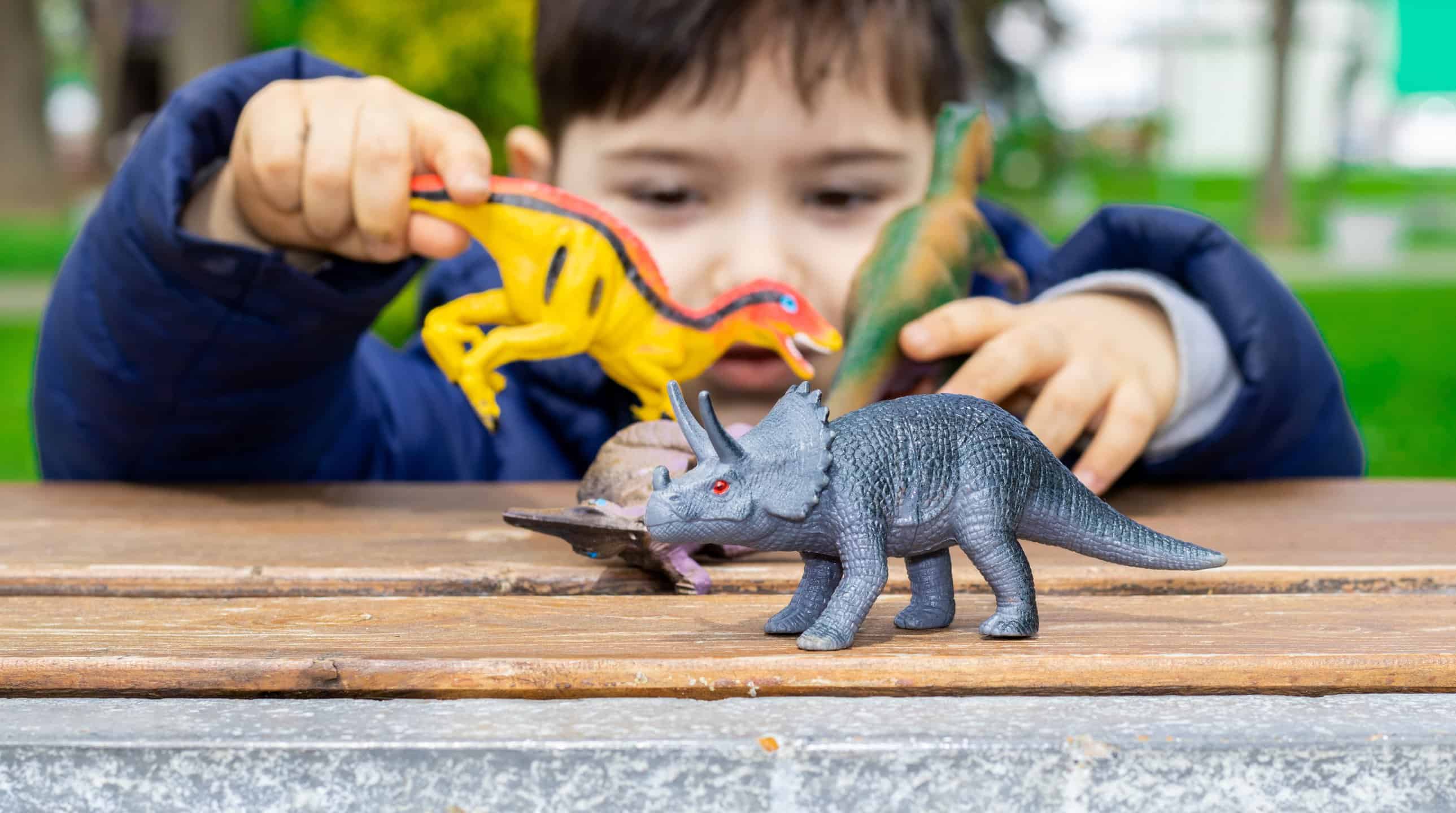Boy plays with dinosaur toys on a table outside
