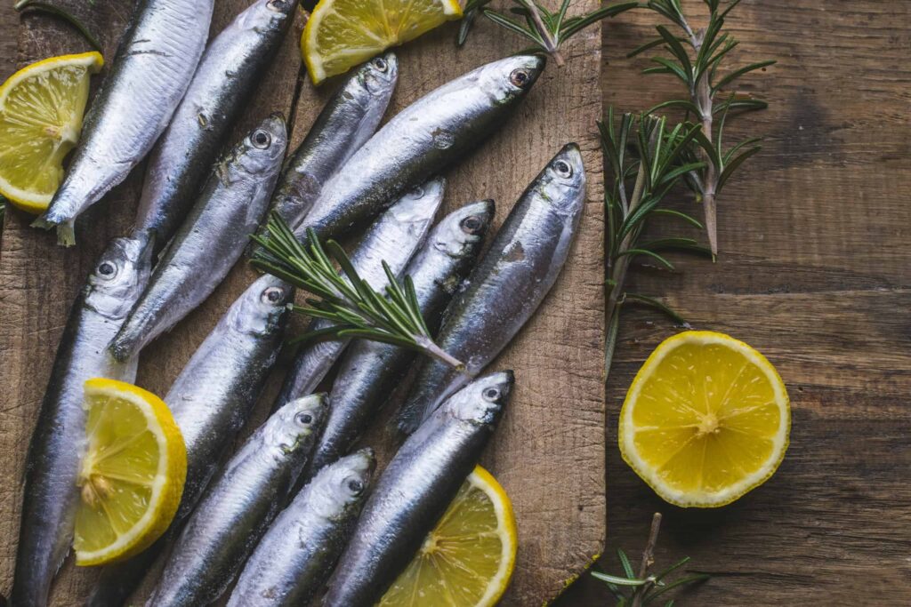 Fresh frozen sardines with lemon and rosemary on old, dark, wooden table