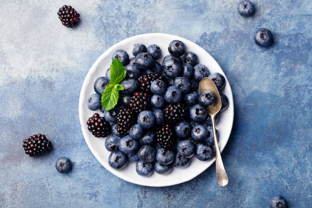 Blueberry and blackberry berries on a white plate on blue stone background. Top view