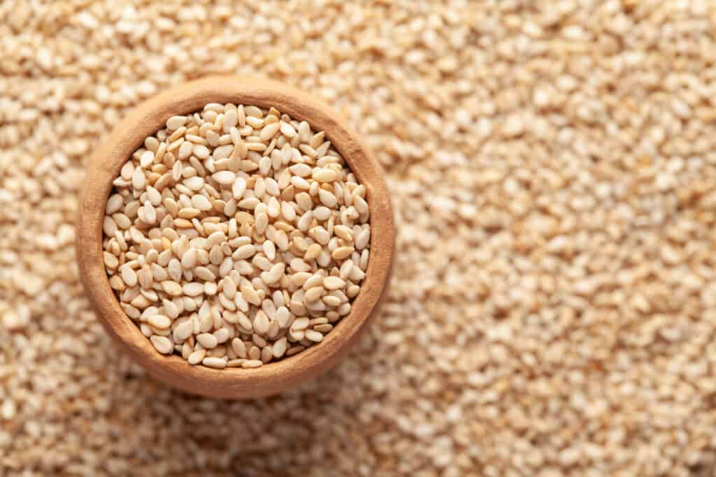 Closeup of sesame seeds on a surface and in an earthen bowl