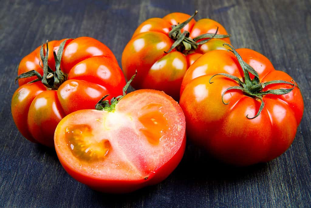 Whole and cut tomatoes on a wood board.