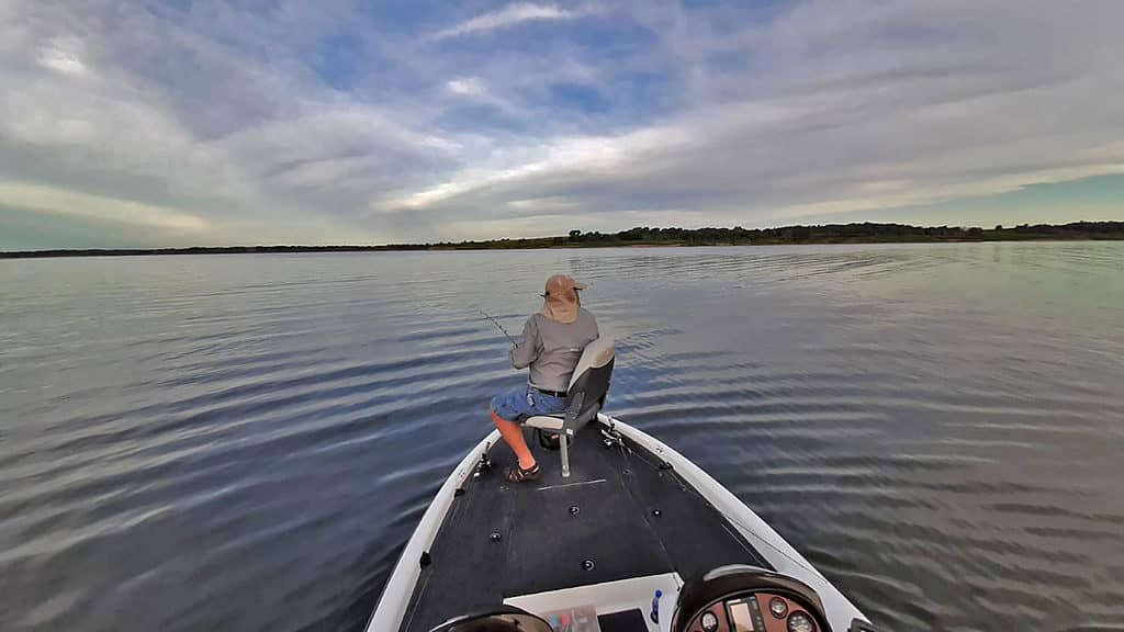 A man stands in a boat at Milford Lake, fishing with a cane pole.