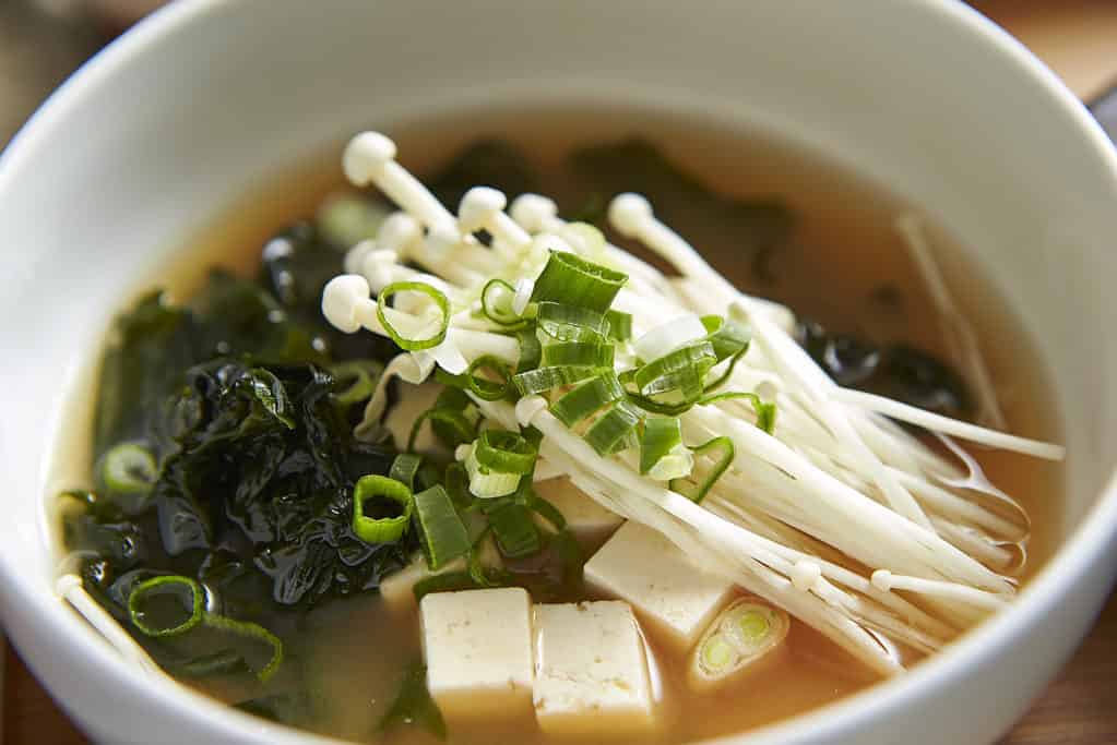 Fresh enoki mushrooms on top of a bowl of tofu and green onion soup