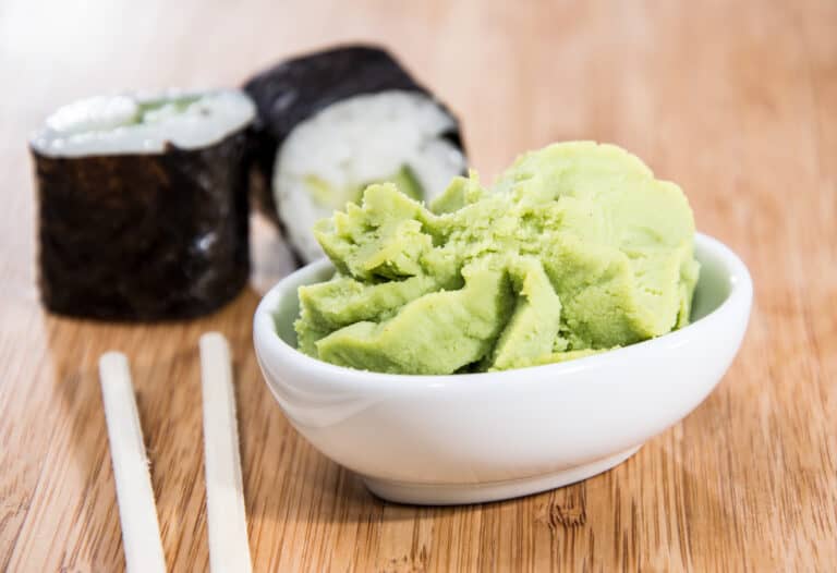 Bwhite bowl of light green wasabi with two California rolls and a pair of chopsticks