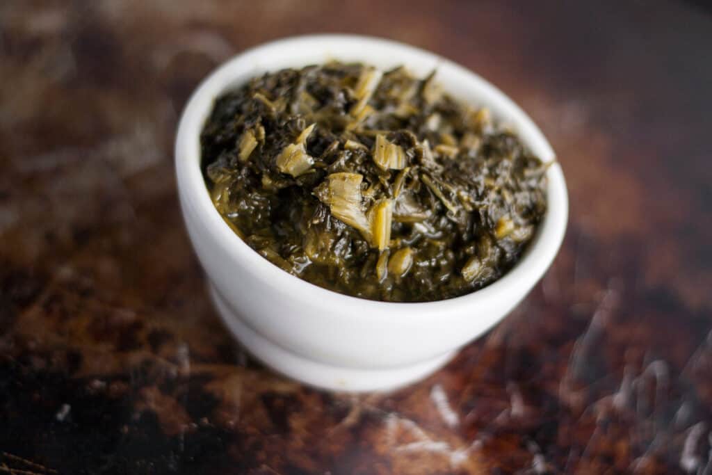 cooked collard greens in a white ceramic bowl on a wooden table.