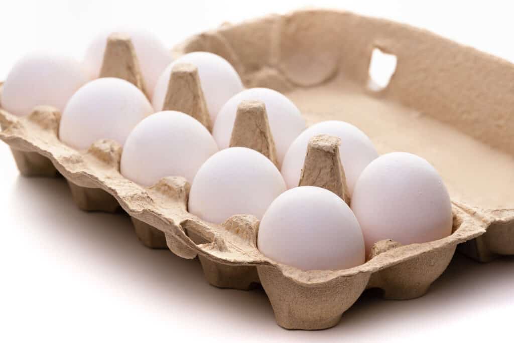 one dozen white chicken eggs, two rows of six, in yellow carton. full frame