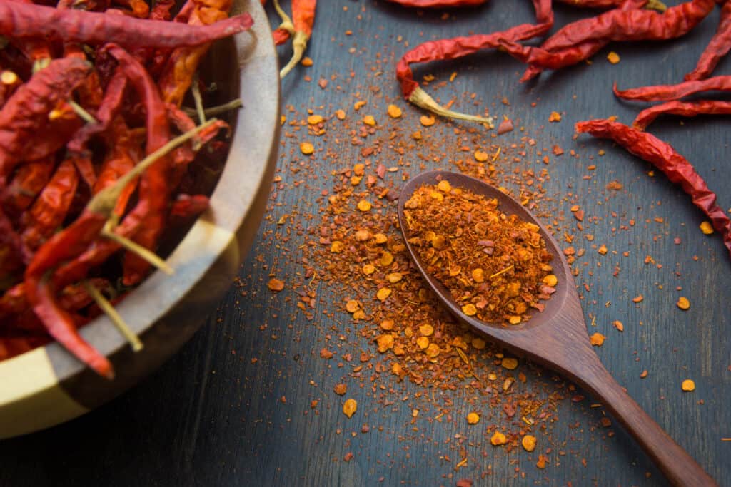 cayenne peppers in a bowl, with ground cayenne in spoon nearby