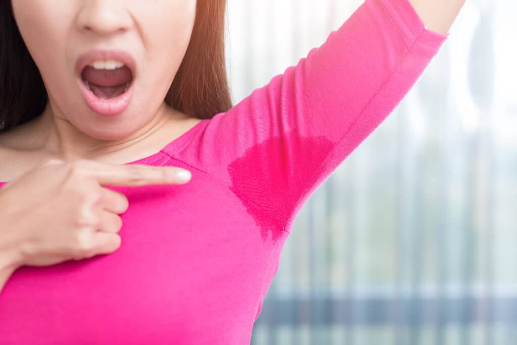 Left frame: female presenting human wearing 3/4 sleeve magenta shirt, with her left arm in the air at an angle toward up right corner of frame, only to elbow is visible. She is using her index of her right hand to point at perspiration stain on her shirt uat her right armpit. Her mouth is open as if she is saying ewwwwww. 