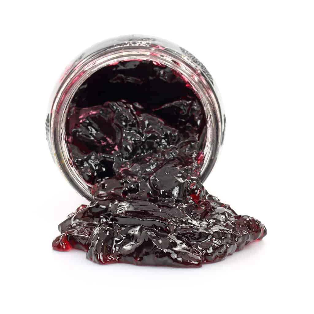 Grape jelly spilling out of a glass jar