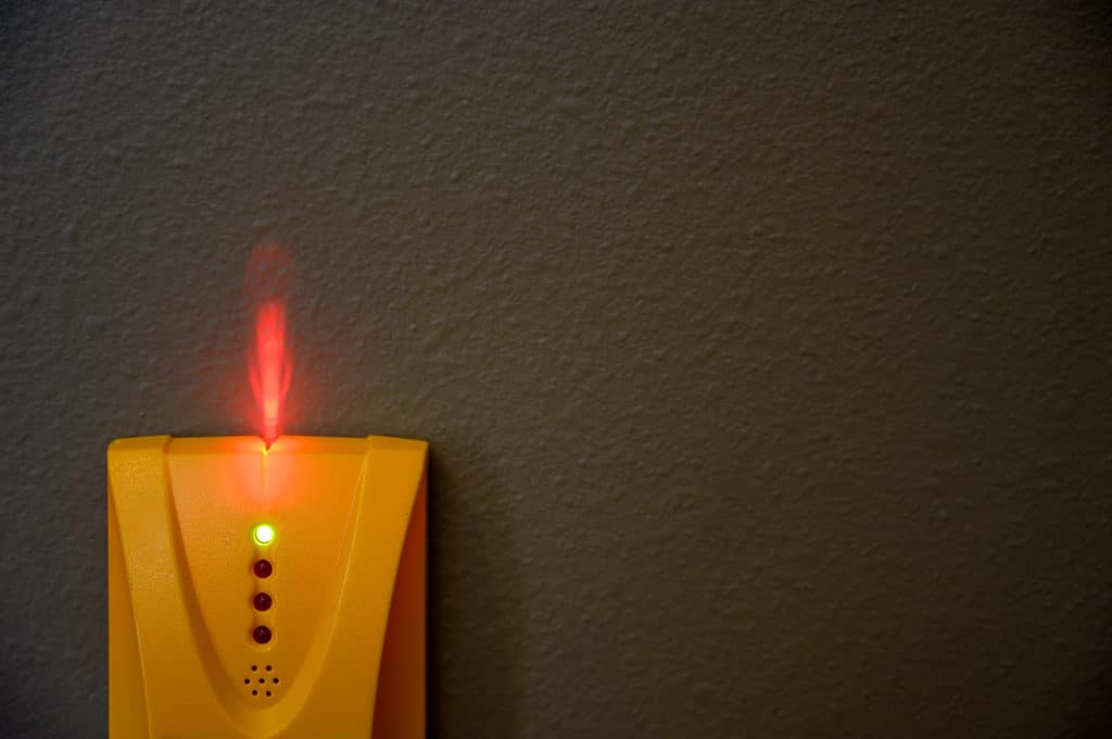 Nền là một bức tường đen than tách biệt: khung dưới cùng bên trái là một công cụ tìm stud điện tử màu cam sáng bằng nhựa.  Có bốn đèn tròn ở trung tâm của công cụ tìm stud, đèn trên cùng được chiếu sáng màu xanh lá cây.  Bên dưới đèn là một vòng tròn bao gồm sáu lỗ nhỏ với một lỗ nhỏ ở trung tâm.  Một ngọn lửa đỏ tươi như ánh sáng đang bắn ra từ đỉnh của công cụ tìm đinh tán lên bức tường đen như than.