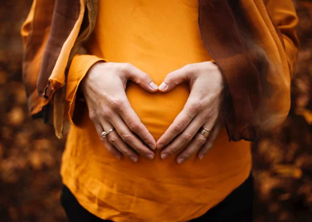 pregnant woman holding hands in heart shape over belly