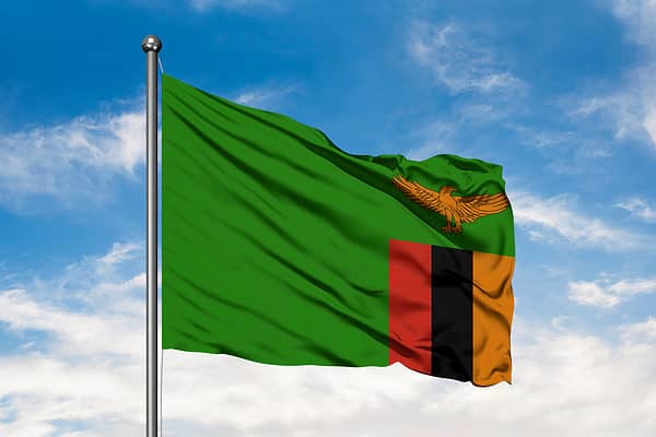 Flag of Zambia waving in the wind against white cloudy blue sky. Zambian flag.