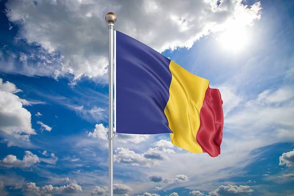 Realistic flag. 3D illustration. Colored waving flag of Romania on sunny blue sky background.