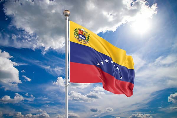 Realistic flag. 3D illustration. Colored waving flag of Venezuela on sunny blue sky background.