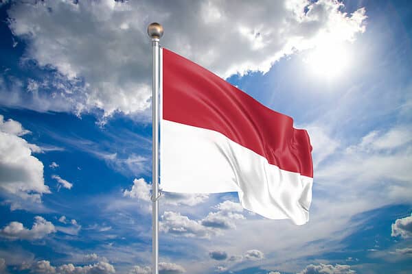 Realistic flag. 3D illustration. Colored waving flag of Indonesia on sunny blue sky background.