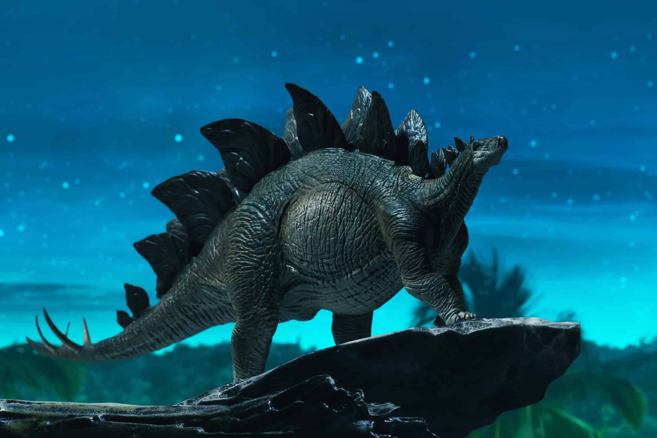 A stegosaurus model stands on a cliff at nighttime. 