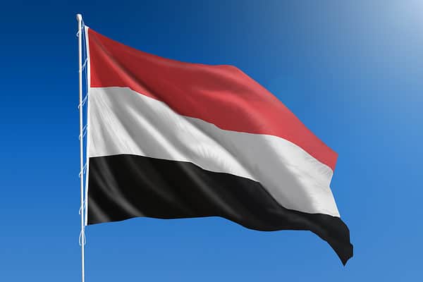 The National flag of Yemen blowing in the wind in front of a clear blue sky