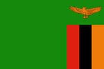 The flag of Zambia consists of a green field with an orange-colored African fish eagle flying above a rectangular block of three vertical stripes of red, black, and orange from left to right