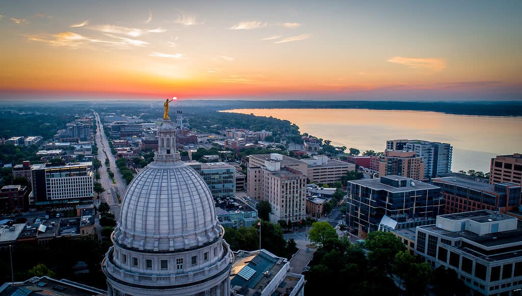 Large photo aérienne d'un lever de soleil spectaculaire et ardent sur le Capitole de l'État du Wisconsin.  La statue au sommet du dôme semble contenir le soleil levant.