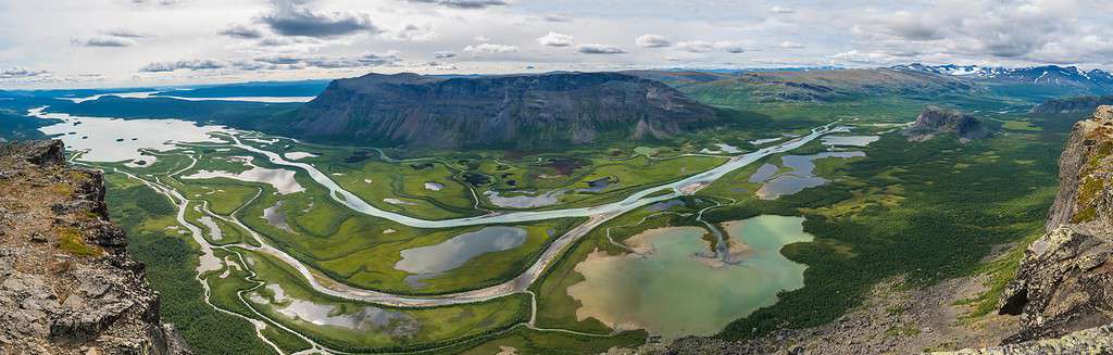 Aerial panoramic scenic view from Skierffe rock summit on glacial Rapadalen river delta valley at Sarek national park with meanders, lakes, mountains, birch trees.