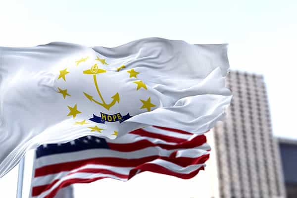 the flag of the US state of Rhode Island waving in the wind with the American flag blurred in the background. Rhode Island was admitted to the Union on May 29, 1790 as 13th state