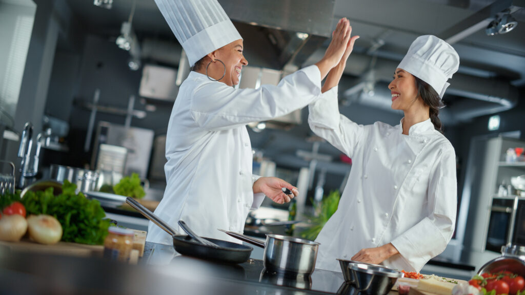 Restaurant Kitchen: Portrait of Asian and Black Female Chefs Preparing Dish, Tasting Food, Doing High-Five in Successful Celebration. Two Professionals Cooking Delicious, Authentic Food, Healthy Meals