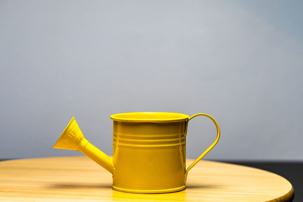 A closeup of a small yellow watering can on wooden table.