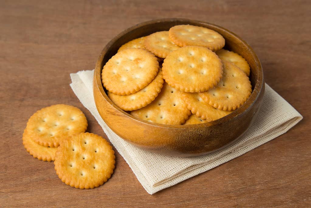 Round salted cracker cookies in wooden bowl putting on linen and wooden background.