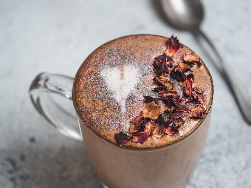 Trendy Coffee with edible glitter and dried rose petals. Cup of sparkly coffee or diamond cappuccino on gray table.