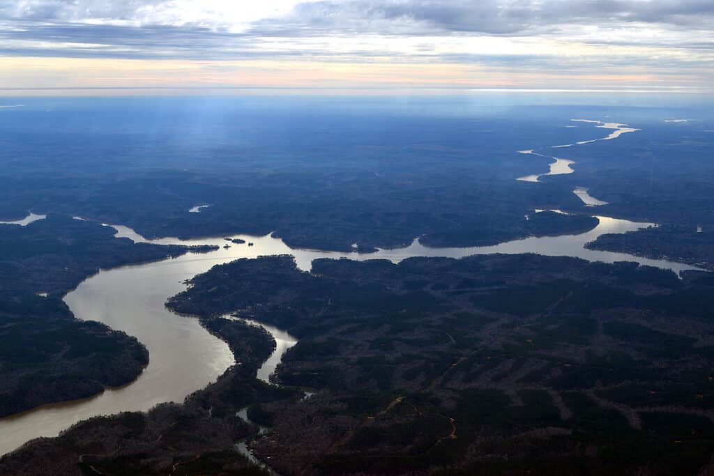 An aerial view of the Coosa River in Alabama. The river is visible meandering through the Fram at a diagonal fro the top right frame to the bottom left frame. The river is surrounded by indistinct vegetation.