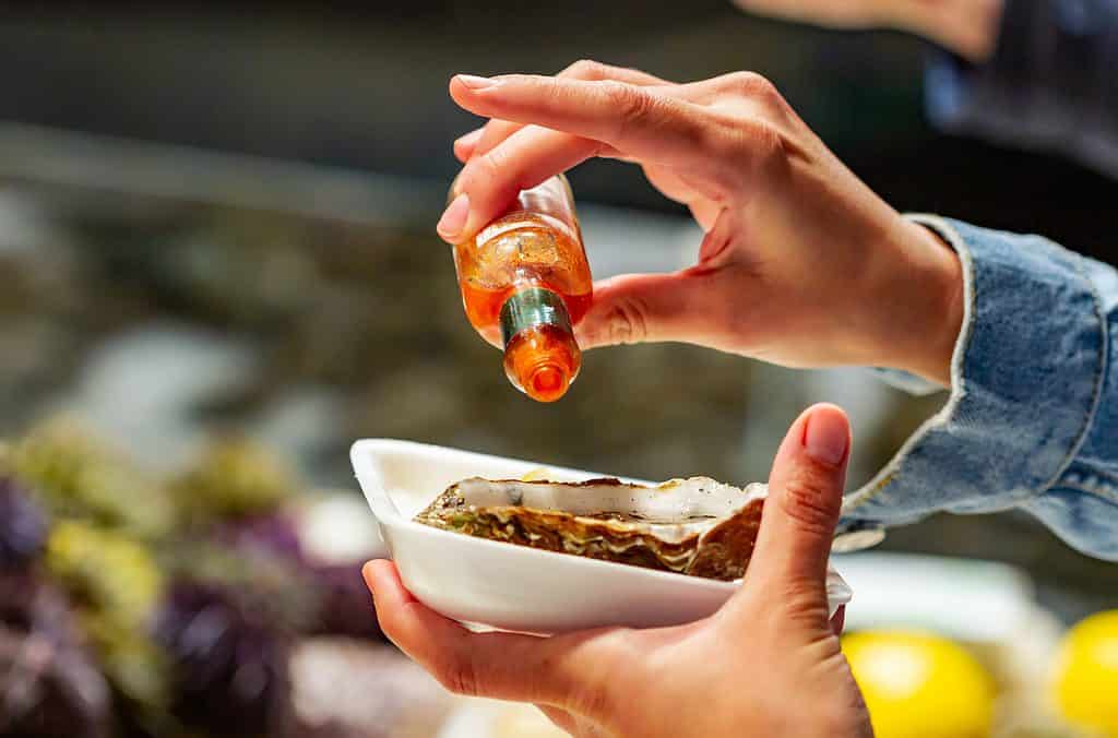 pouring hot sauce on oyster