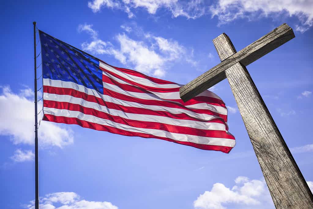 American flag on a brilliant blue sky with a wooden cross