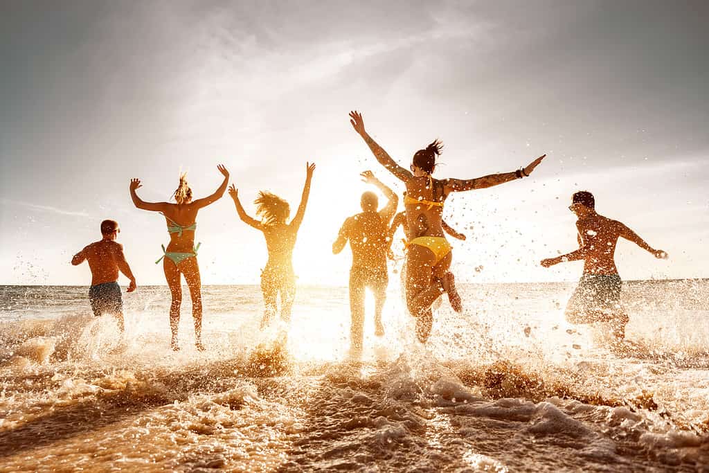 Big group of friends run and jump at sunset sea beach.