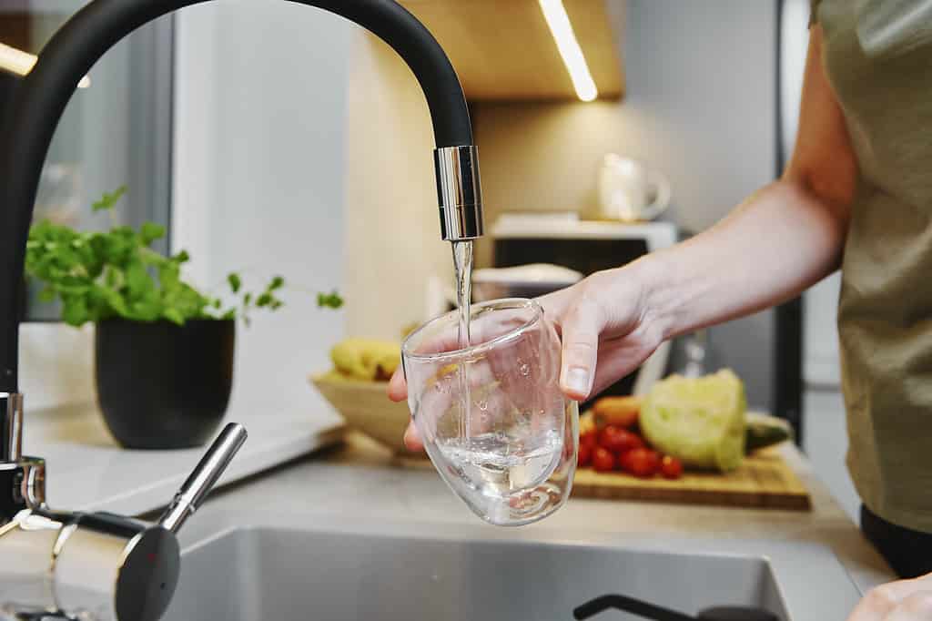 Femme versant de l'eau du robinet dans le verre à la cuisine
