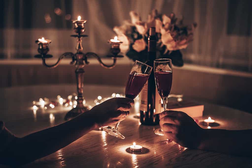 Man and woman with wine glasses in hands having romantic candle light dinner at table at home. Man and woman with glasses of wine in hands. Concept for Valentine's Day or evening date by candlelight.