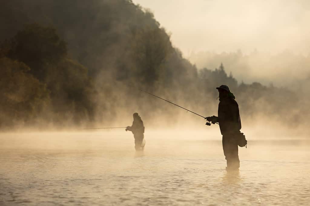 Men fishing in river with fly rod during summer morning. Beautiful fog.