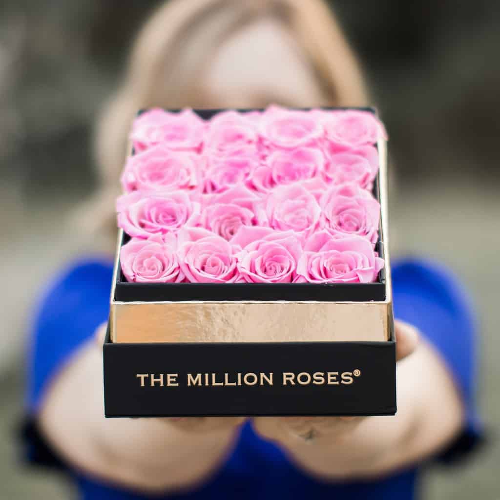 A woman in a blue dress holding a box of pink roses from the Million Roses Company.