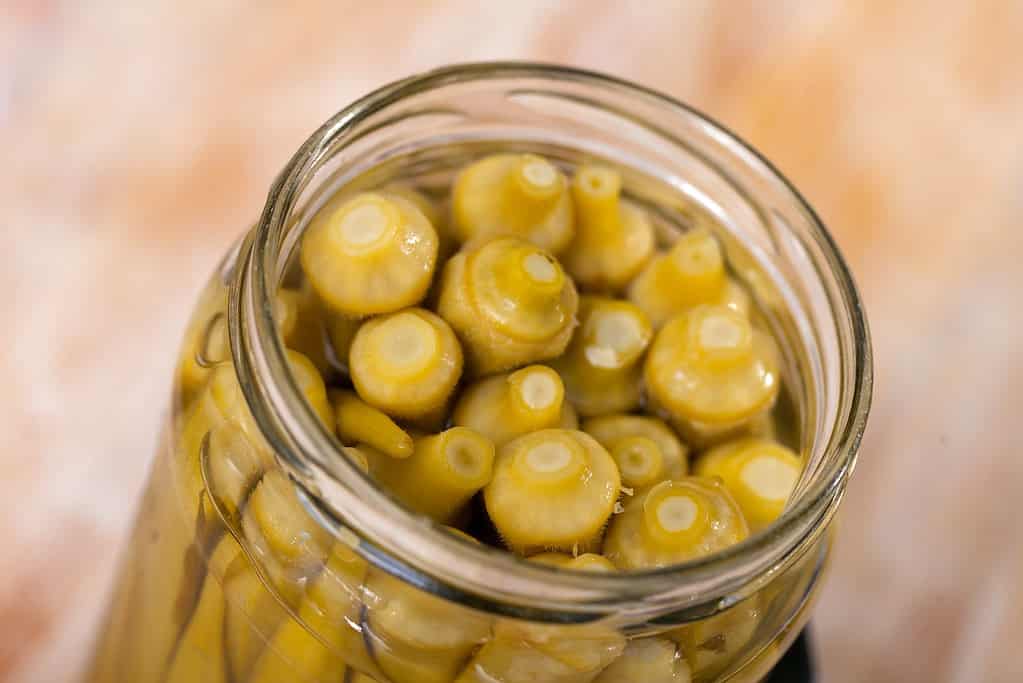 Glass jar with marinated okra on wooden table