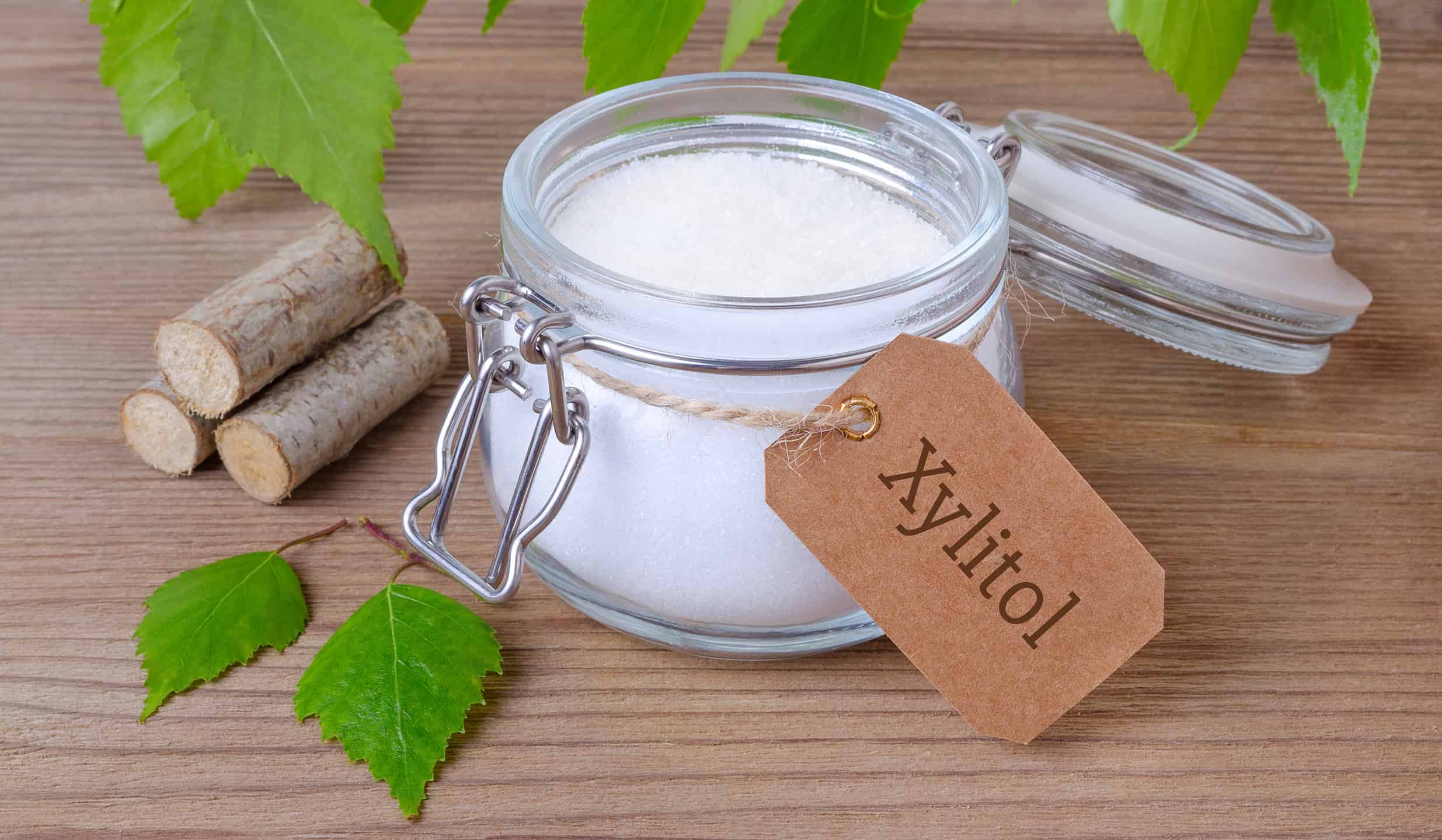 sugar substitute xylitol, a glass jar with birch sugar, liefs and wood on wooden background