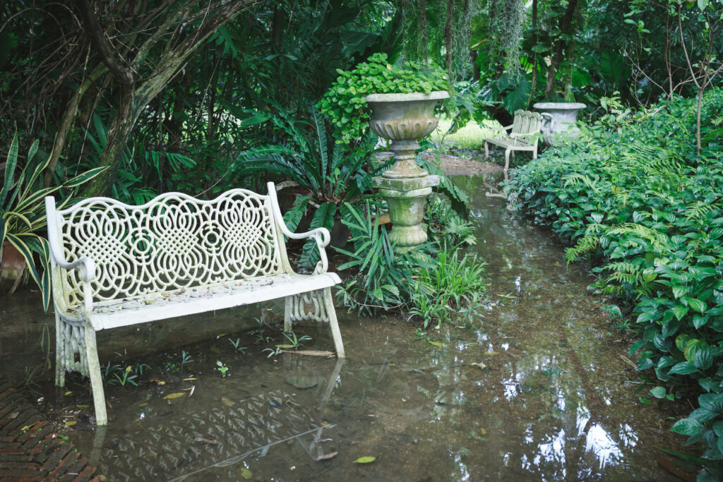White chair in waterlogged outdoor garden, full of trees and bushes.