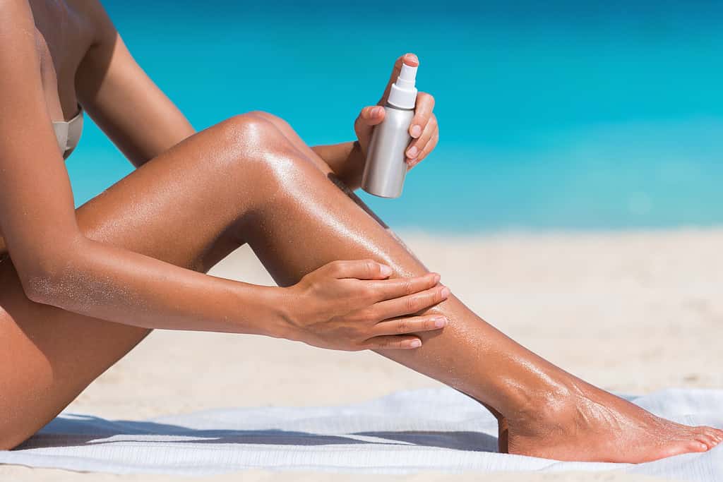 Woman spraying sunscreen on her leg- Best UV index to tan