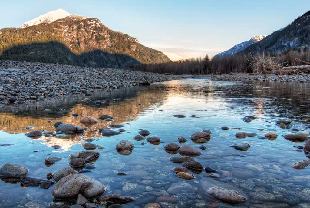 Clear river with rocks leads towards mountains lit by sunset