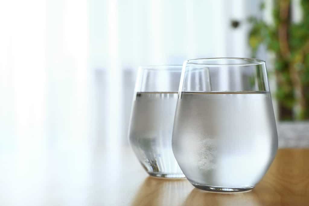 Glasses full of water on wooden table in room, space for text. Refreshing drink