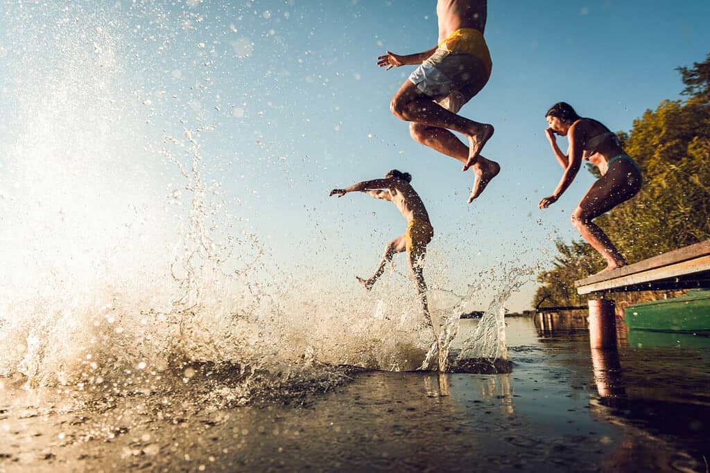 Friends having fun enjoying a summer day swimming and jumping at the lake.